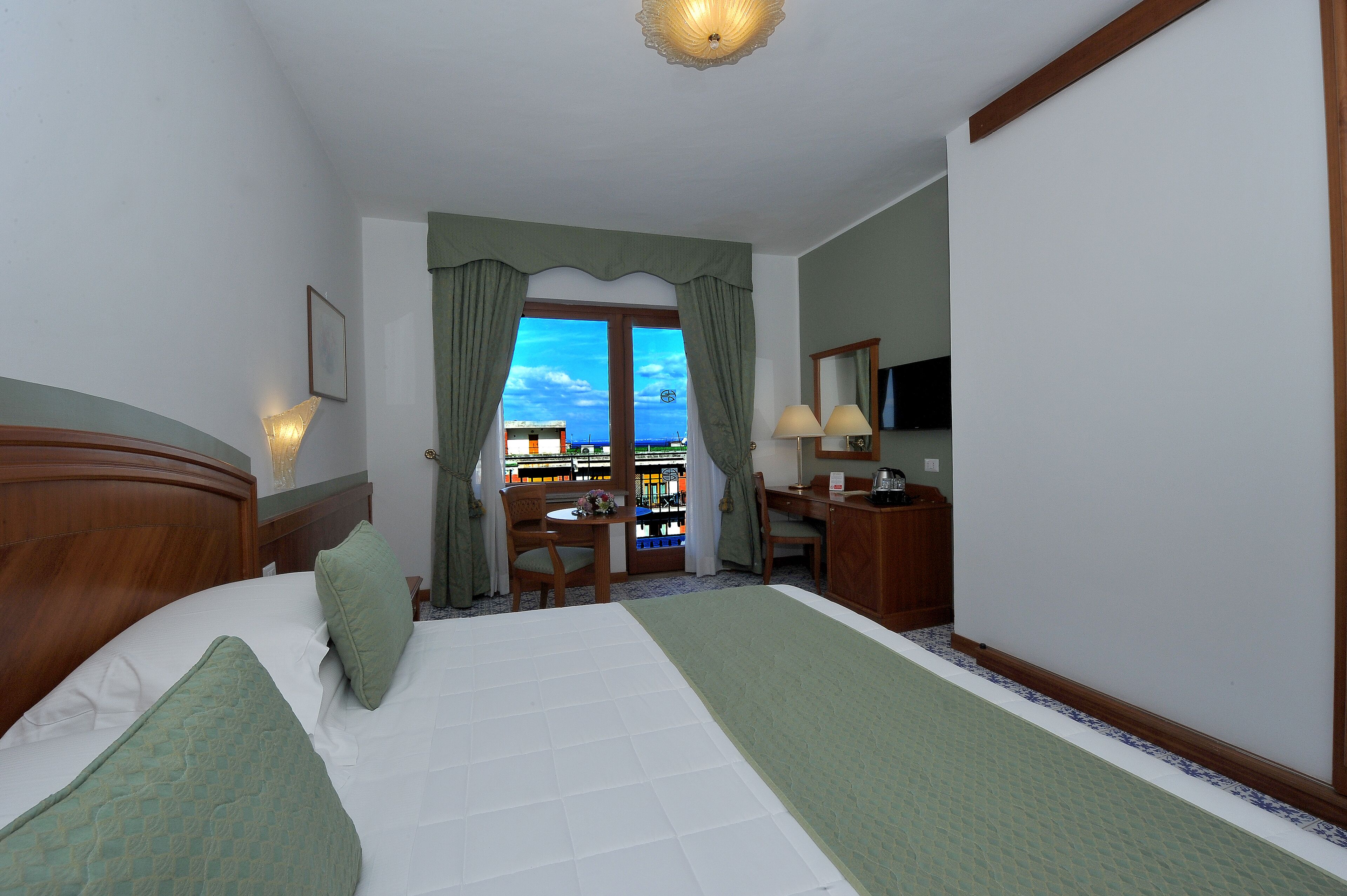 Habitación de hotel con cama, escritorio, silla, televisión y vista al mar por la ventana.