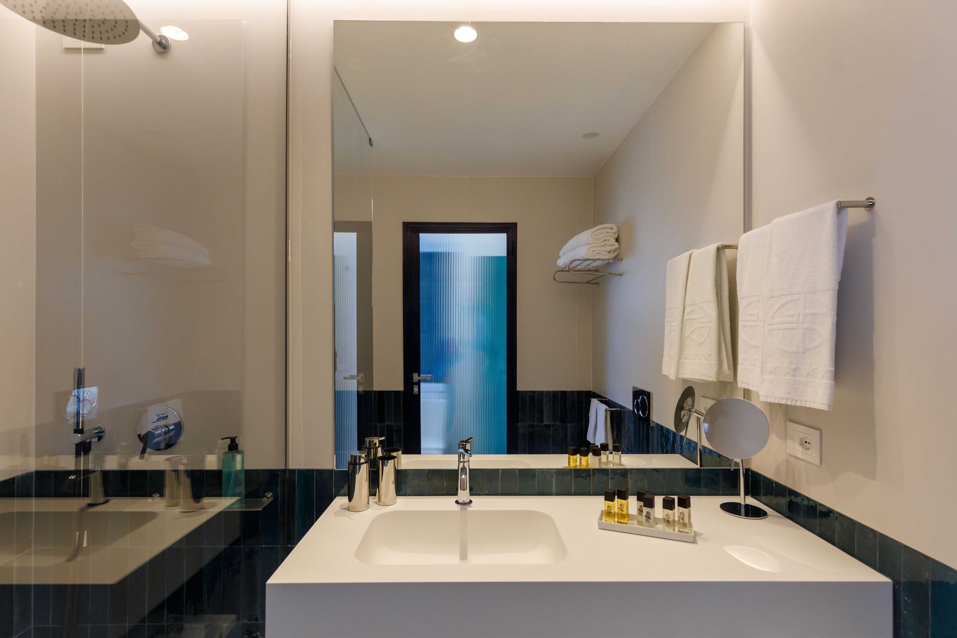 Un baño moderno con un espejo grande, un lavamanos blanco y una ducha con mampara de vidrio.