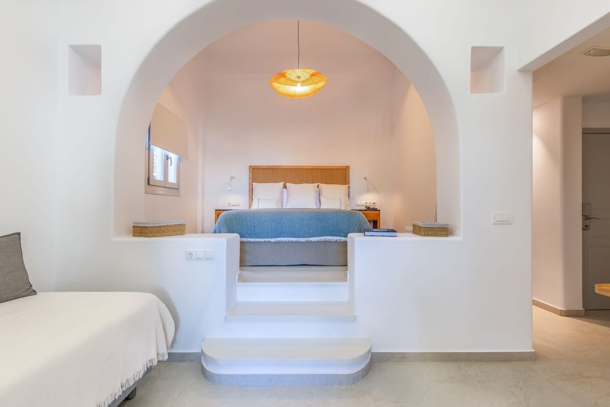 A bedroom with a bed, a desk, a chair, a lamp, and a staircase leading to an upper level.