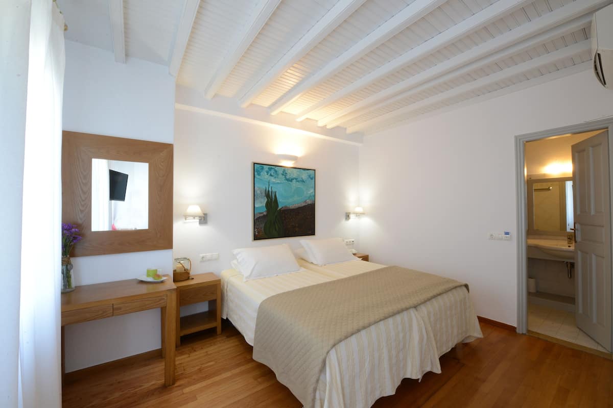 A bedroom with a bed, bedside table, lamp, painting, and a door leading to a bathroom.