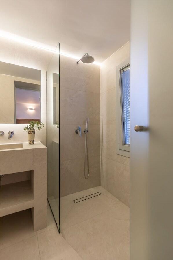 Un baño moderno con cabina de ducha de vidrio, un lavabo con planta y una ventana con persianas.