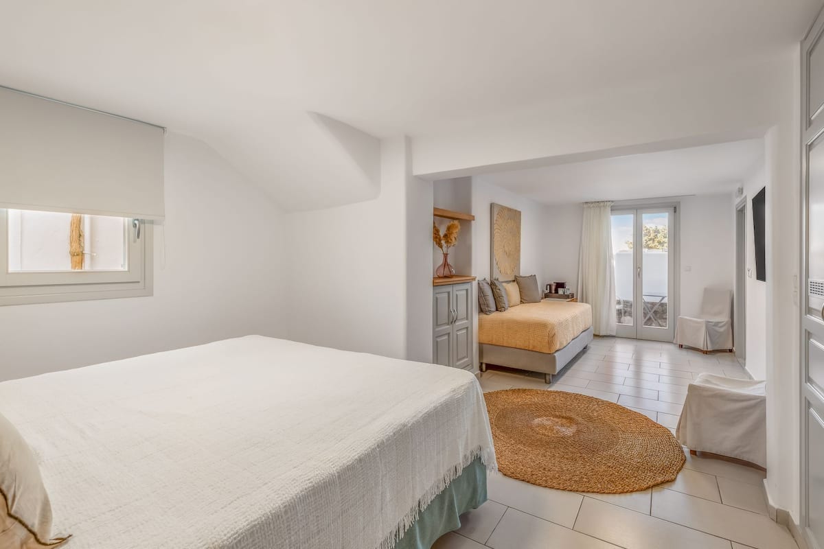 A bedroom with a bed, a small desk, a chair, a window, and a sliding glass door leading to a balcony.