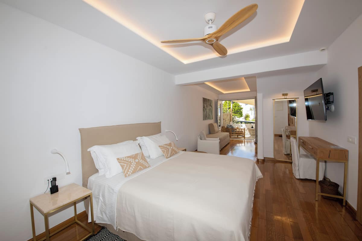 A modern bedroom with a large bed, a ceiling fan, a desk, and a TV.