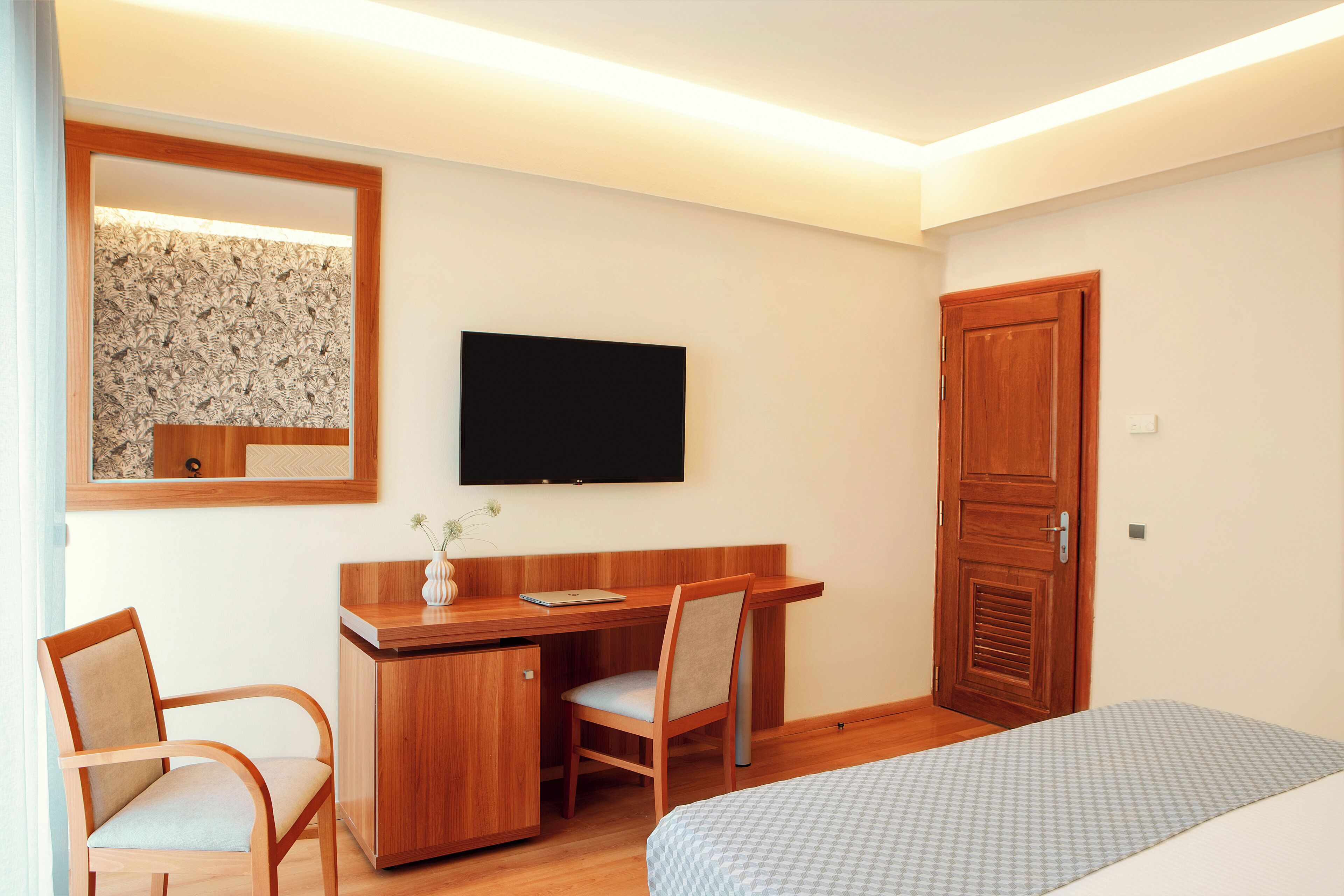 Quarto de hotel com escrivaninha de madeira, uma cadeira, uma cama, televisão e guarda-roupa.