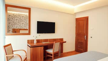 A hotel room with a wooden desk, a chair, a bed, a television, and a wardrobe.