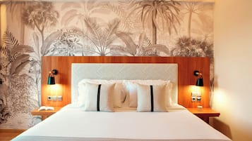 Habitació d'hotel amb un llit gran, dues taules de nit, un taulell, una paret amb un mural tropical i dues làmpades penjades a la pared.