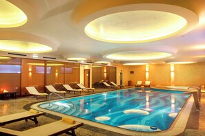 A hotel swimming pool with lounge chairs and a circular ceiling design.