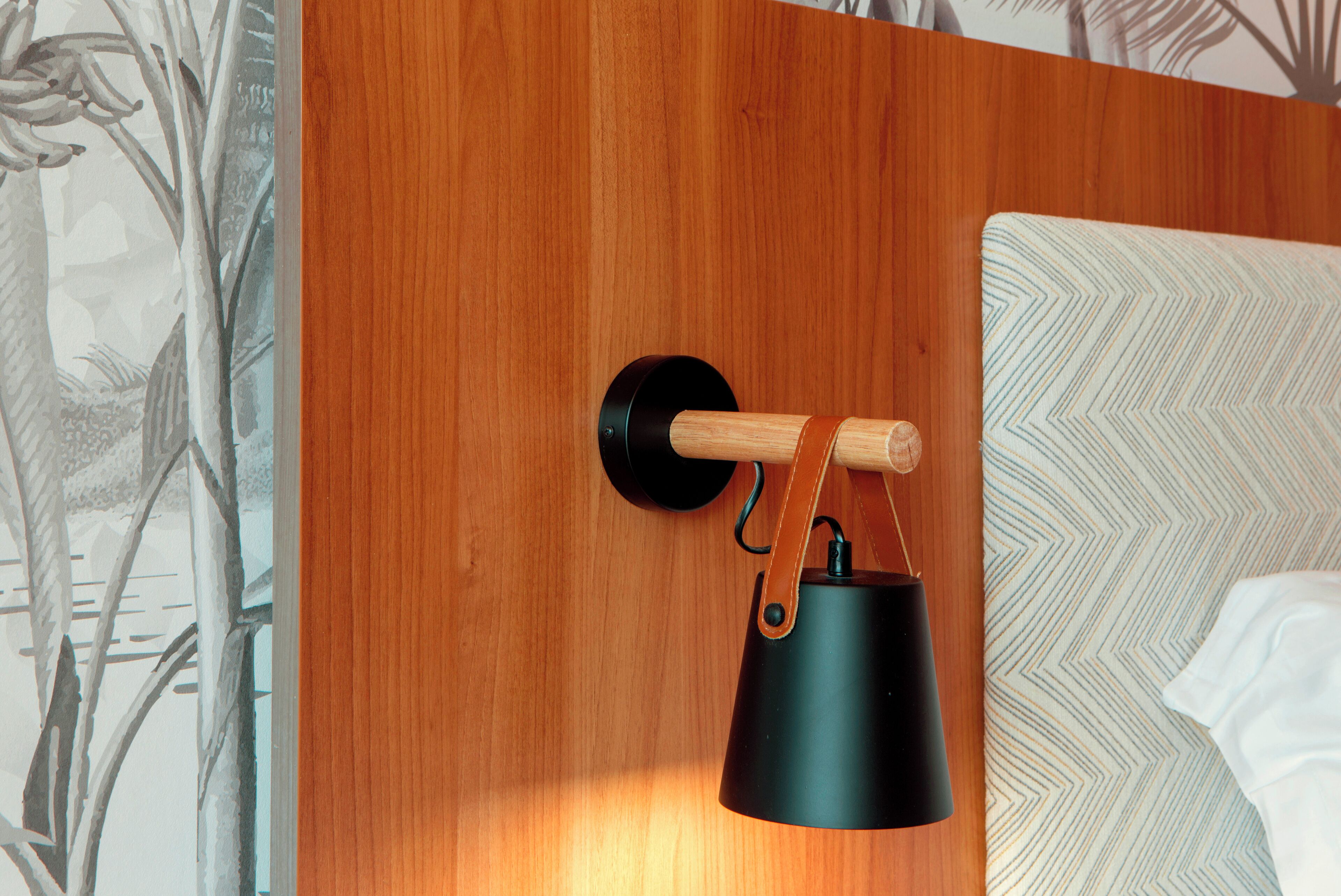 En træsenggavl med en sort lampe og en pude med et chevronmønster.