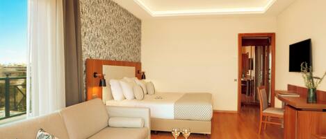 A modern hotel room with a sofa, a bed, a dining table with a plate of food, and a TV mounted on the wall.
