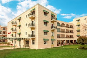 A multi-story hotel with balconies, a covered entrance, and a well-maintained lawn.