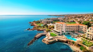 A coastal hotel with a pool, multiple balconies, and a view of the sea. - Zeus Essence Ramada by Wyndham Athens (Marathon)