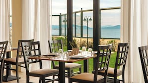 A dining area with a view of the sea, featuring a table set for four with chairs, a potted plant, and a salt and pepper set. - Zeus Essence Ramada by Wyndham Athens (Marathon)