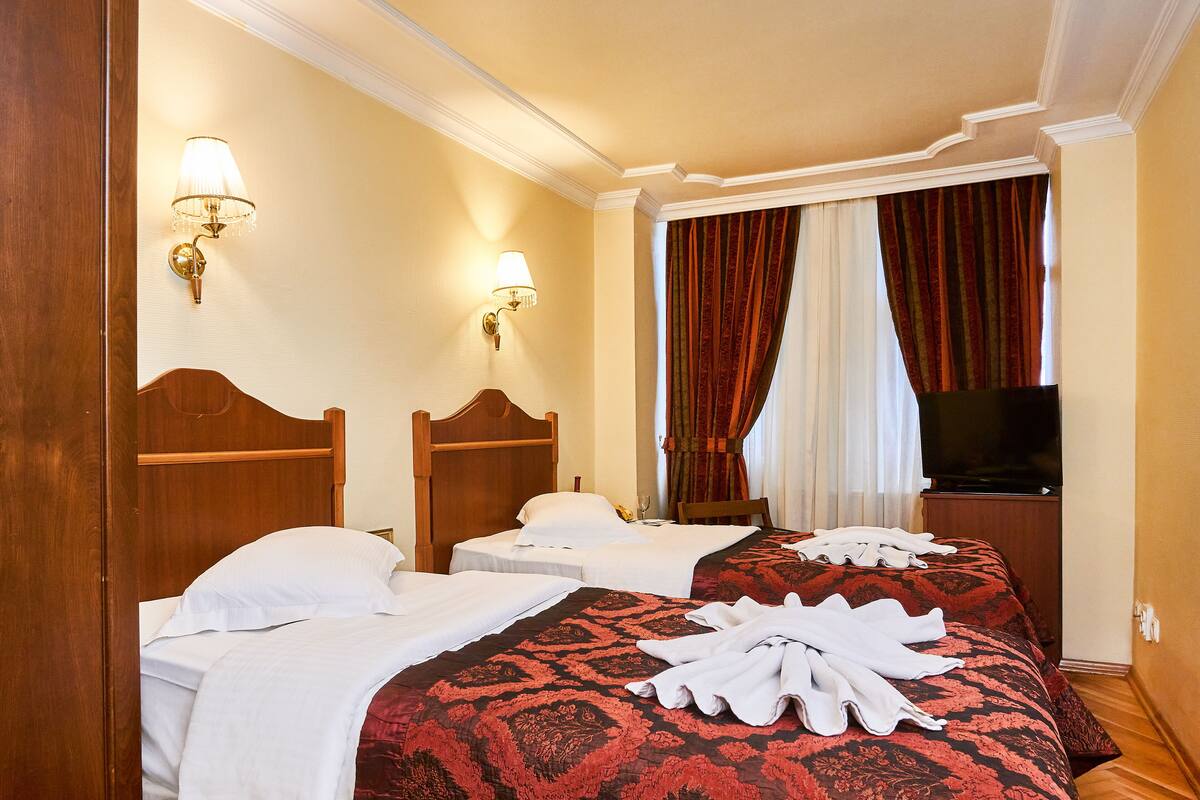 A hotel room with two beds, a television, and a window with curtains.