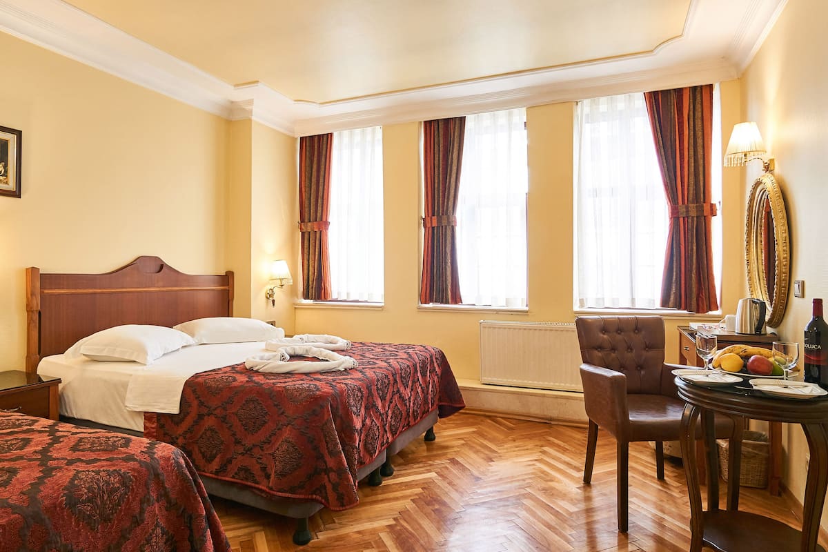 A hotel room with two beds, a dining table with a fruit bowl, a chair, and a lamp.