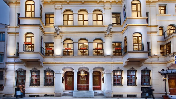 Un edificio de varios pisos con ventanas arqueadas y balcones, que presenta una entrada imponente con una puerta de madera y escalones que la conducen.