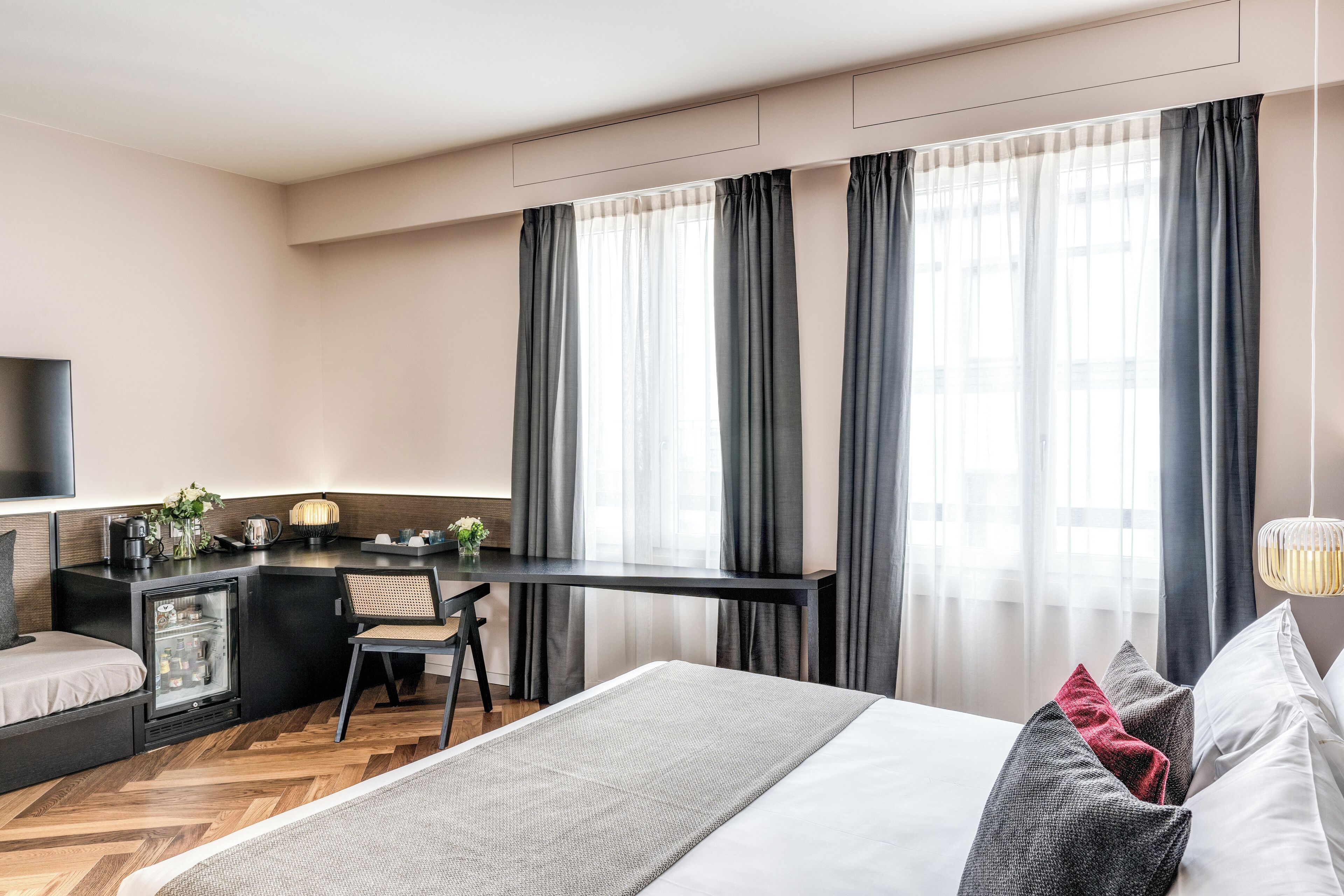 Et moderne hotelværelse med seng, skrivebord, lille køleskab og fjernsyn.