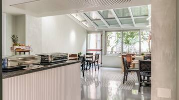 Eine moderne Küche mit einer zentralen Kochinsel, einem Essbereich mit Stühlen und einem Tisch sowie großen Fenstern mit Blick auf Grünflächen.