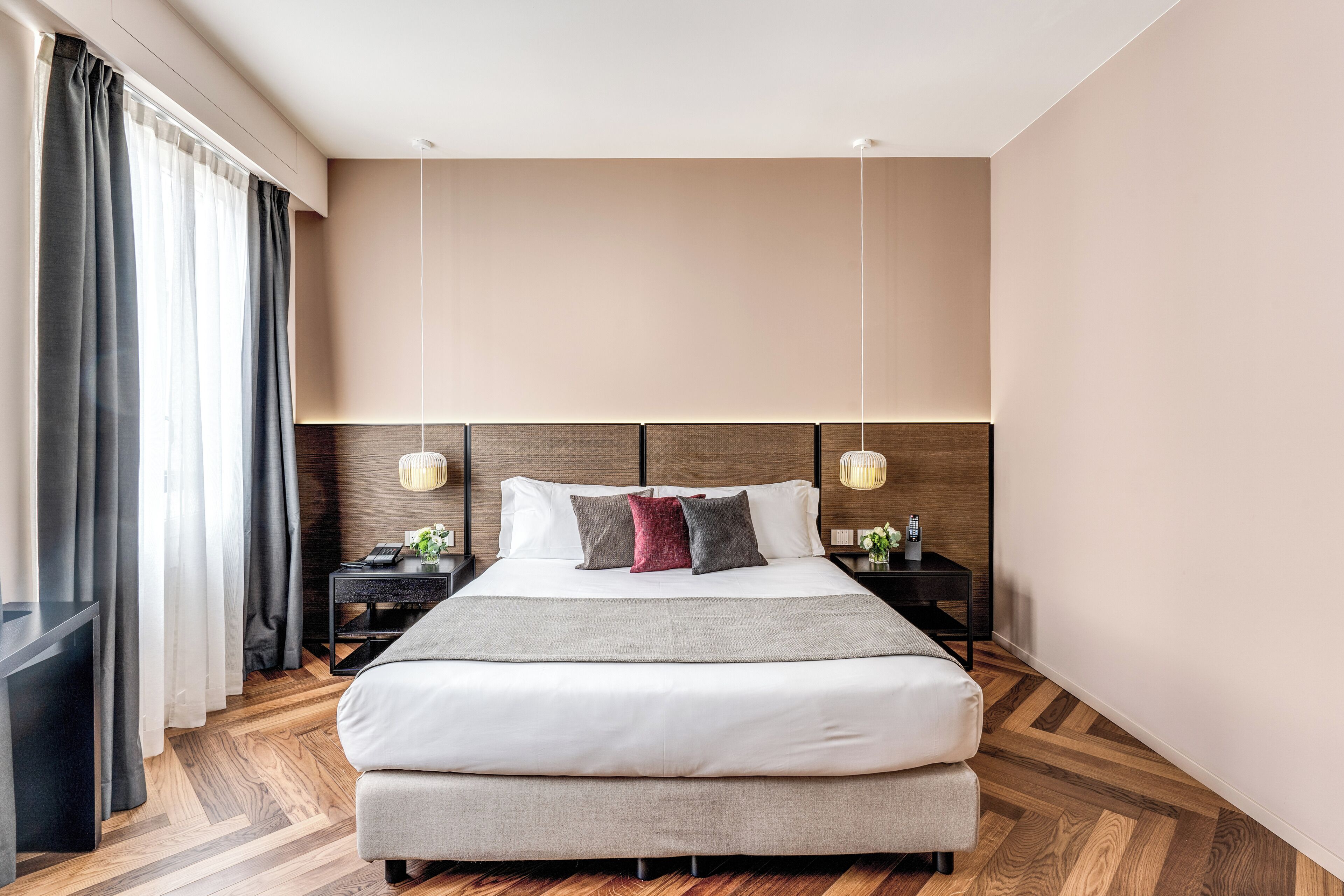 A modern hotel room with a large bed, wooden flooring, and a neutral color scheme.