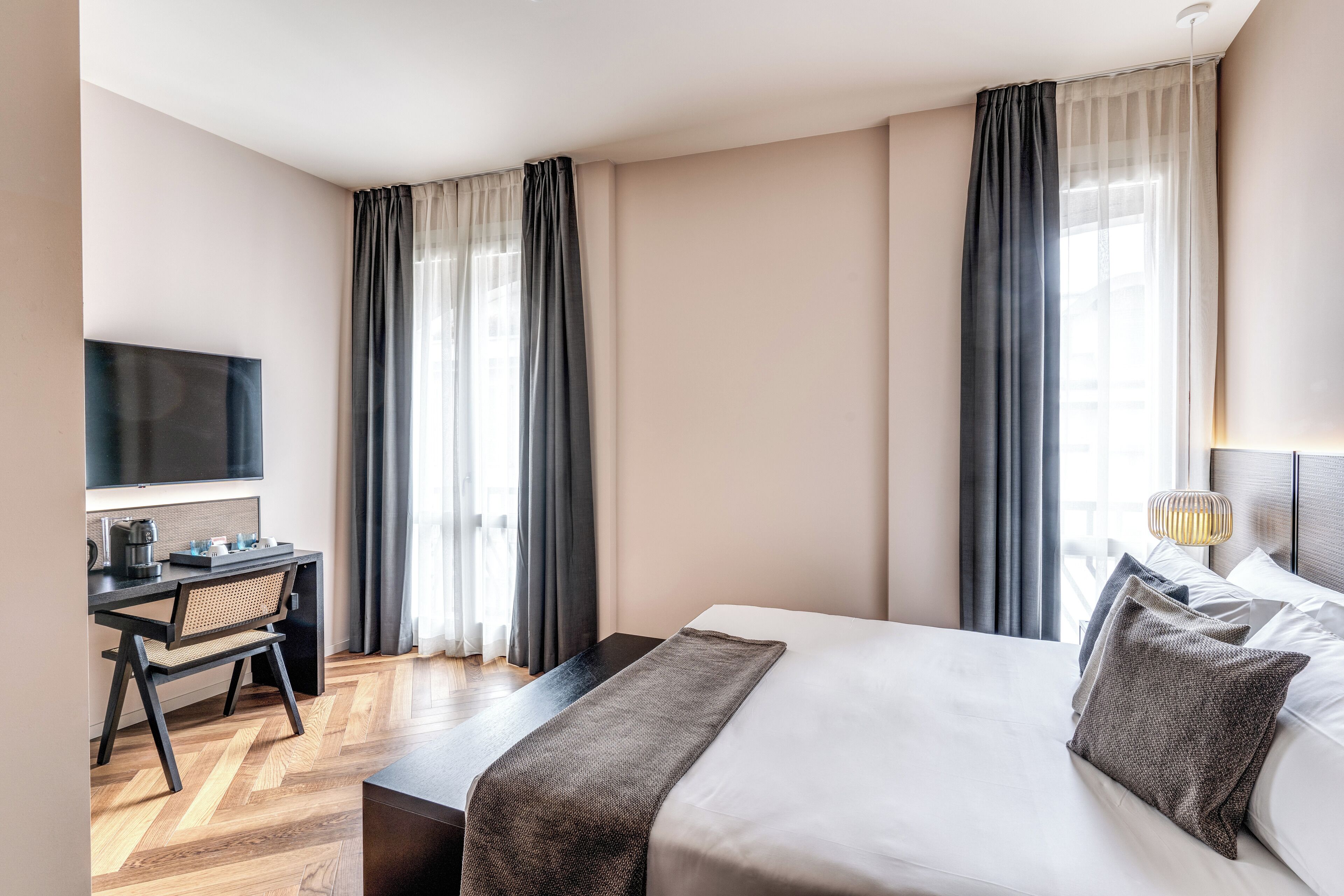A hotel room with a bed, a desk with a chair, a television, and a window with curtains.