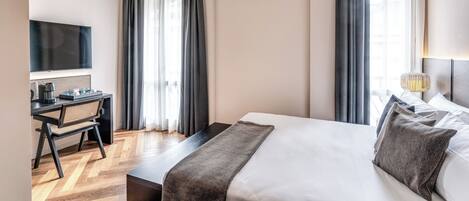 A hotel room with a bed, a desk with a chair, a television, and a window with curtains.