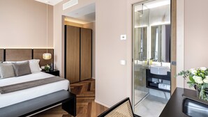 A modern bedroom with a large bed, a bedside table with a lamp, a wooden wardrobe, and a bathroom with a sink and mirror. - Plinius Lifestyle Hotel Lake Como (Como)