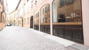 A narrow street with buildings on both sides, featuring large windows and a paved walkway. - Plinius Lifestyle Hotel Lake Como (Como)