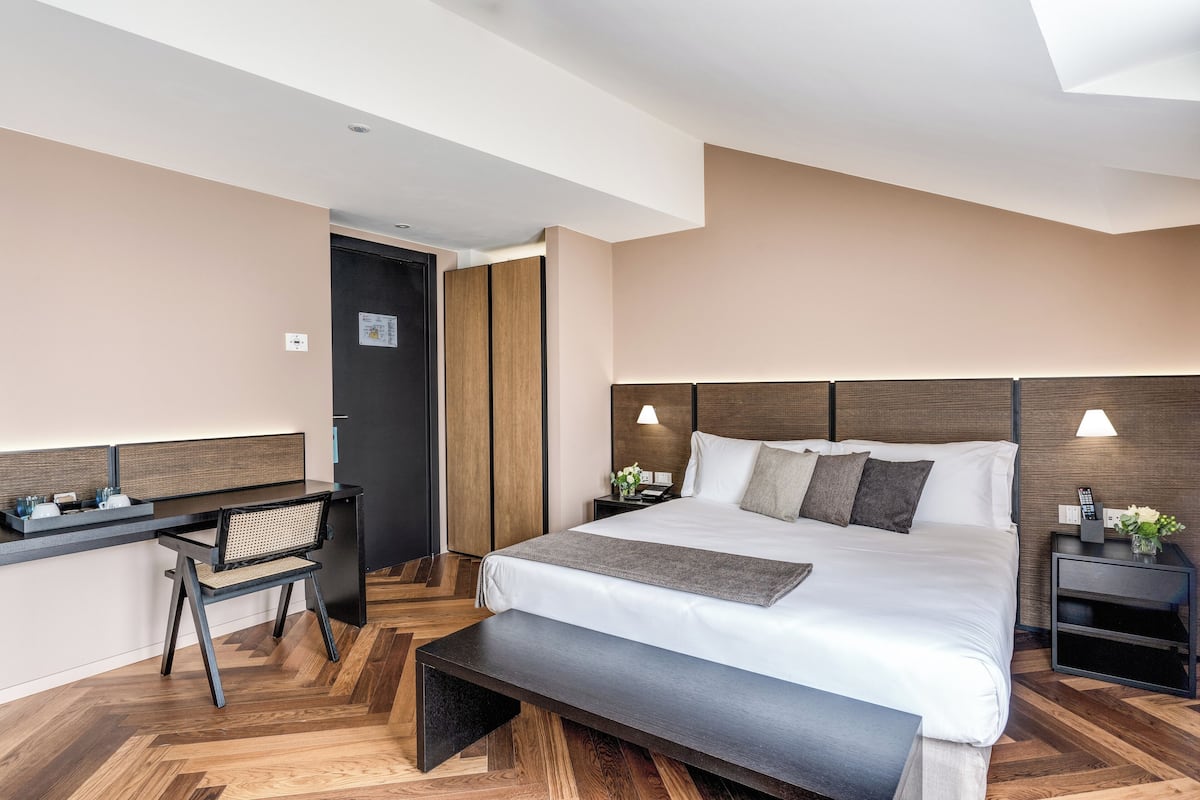 A modern hotel room with a large bed, a desk, and a bench.