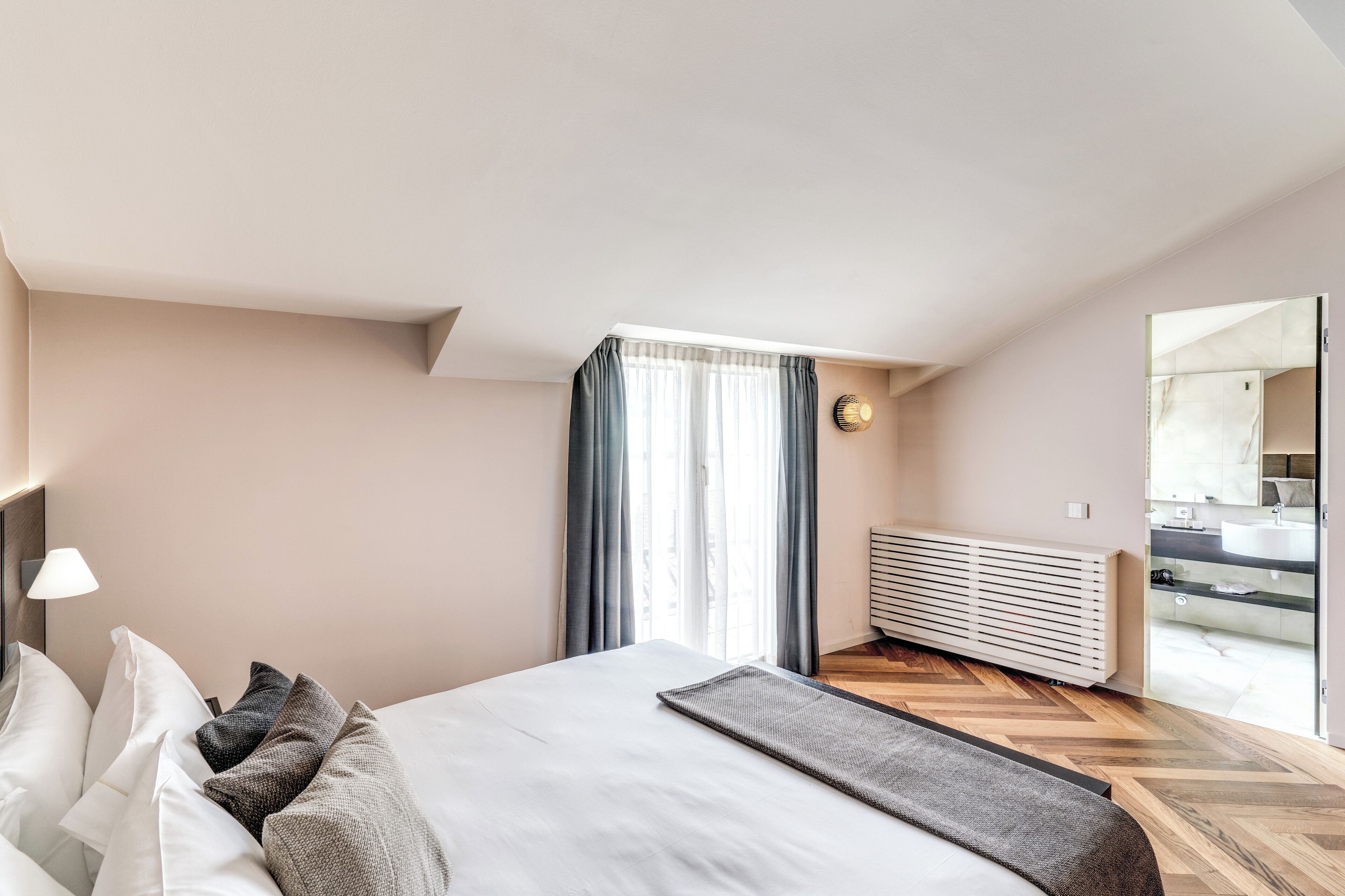 A modern hotel room with a large bed, a view of the bathroom, and a wooden floor.
