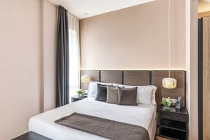 Une chambre d’hôtel moderne avec un grand lit, une table de chevet avec une lampe et une petite table de nuit avec une télécommande.