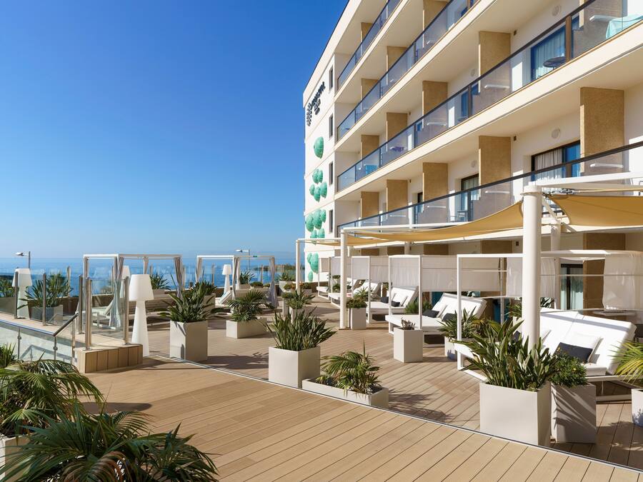 A multi-story hotel with outdoor seating areas, potted plants, and a view of the sea.