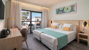 Habitación de hotel con cama, escritorio, silla, cafetera y vista al exterior.