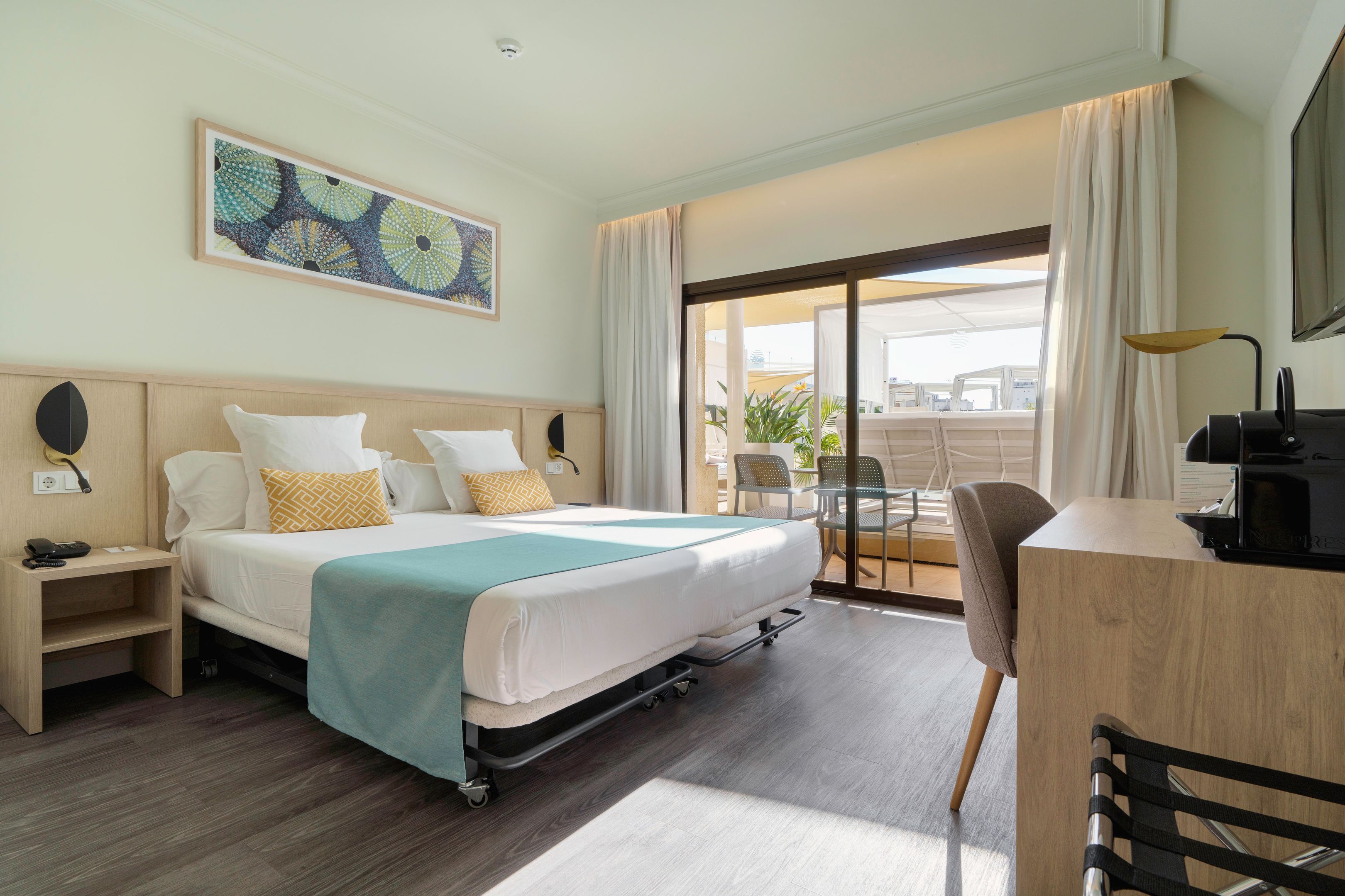 A hotel room with a bed, a desk, a chair, a TV, and a balcony with a view.