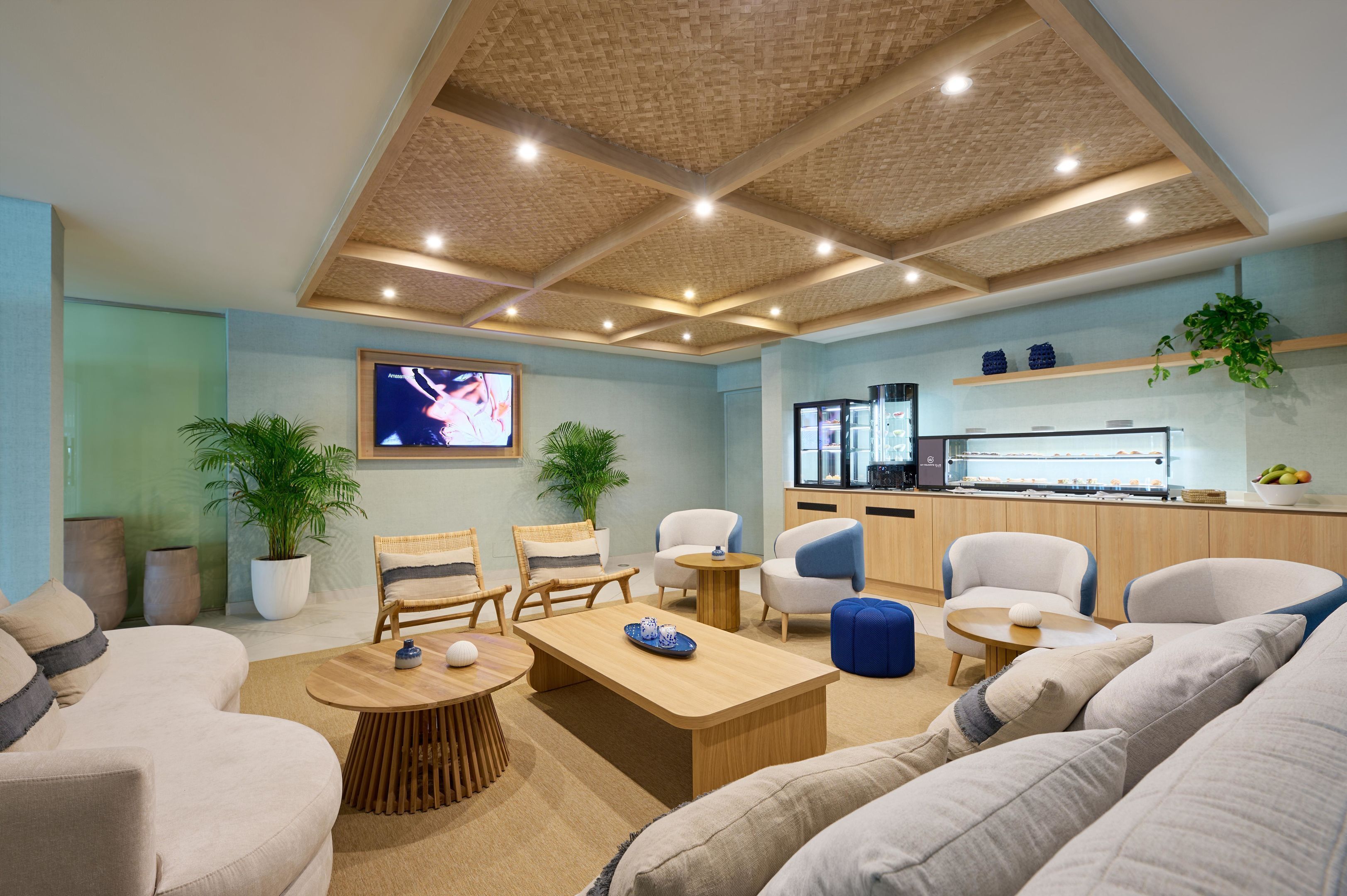 A modern living room with a wooden ceiling, a television, seating, and a kitchen area.