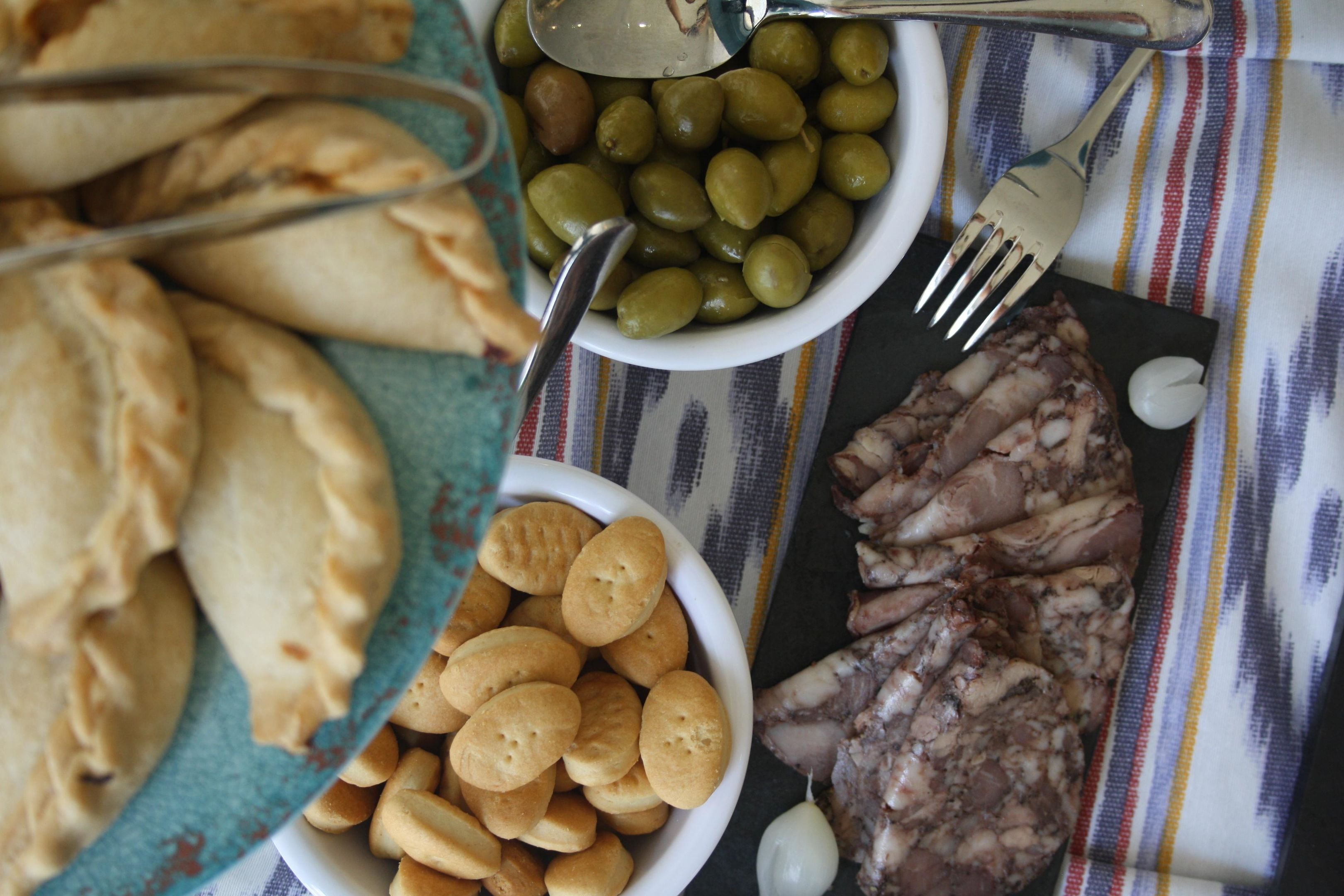 A table with a variety of food items including olives, biscuits, and sliced meat.