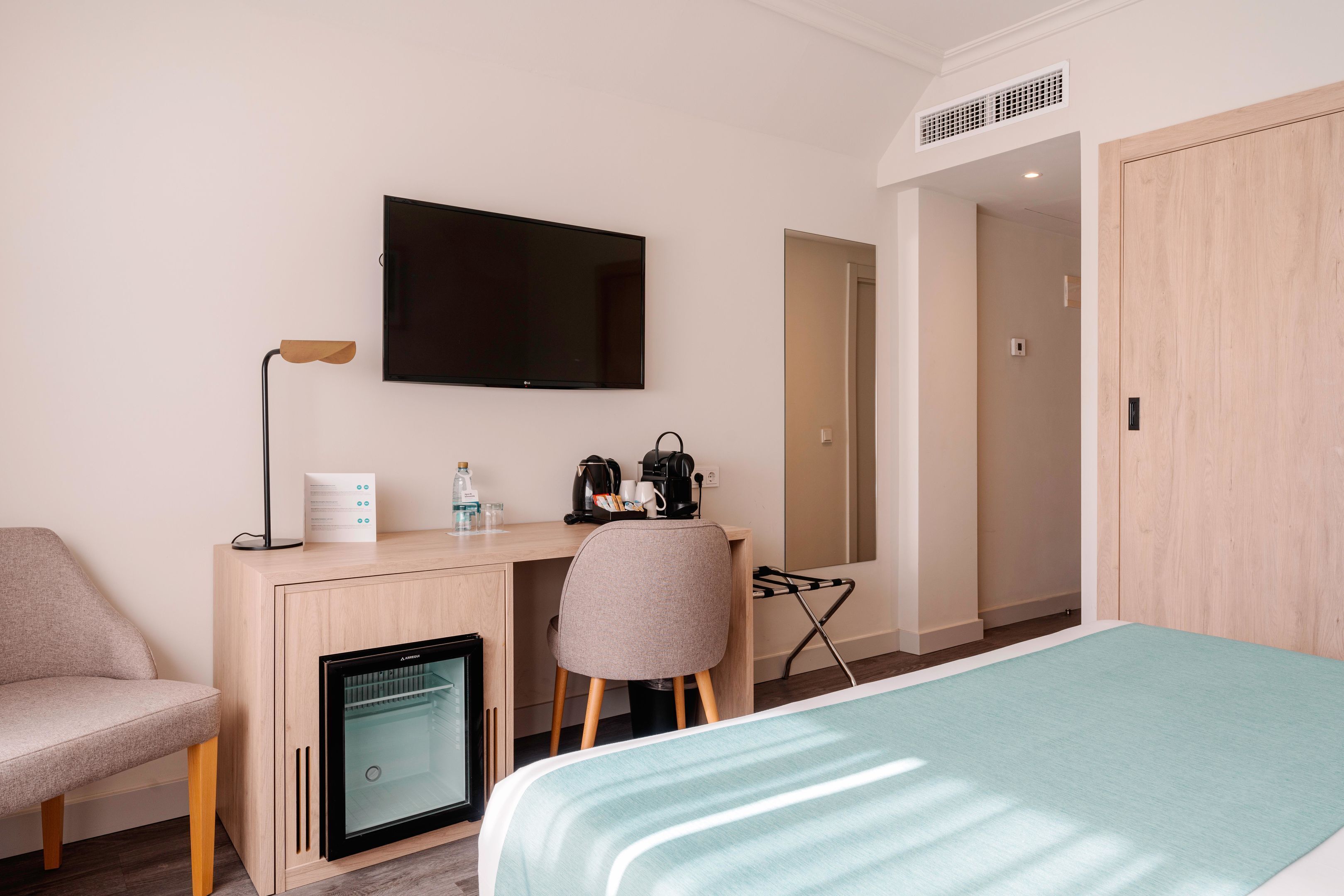 Ein Hotelzimmer mit Bett, Schreibtisch mit Stuhl, Fernseher, Minikühlschrank und Kleiderschrank.