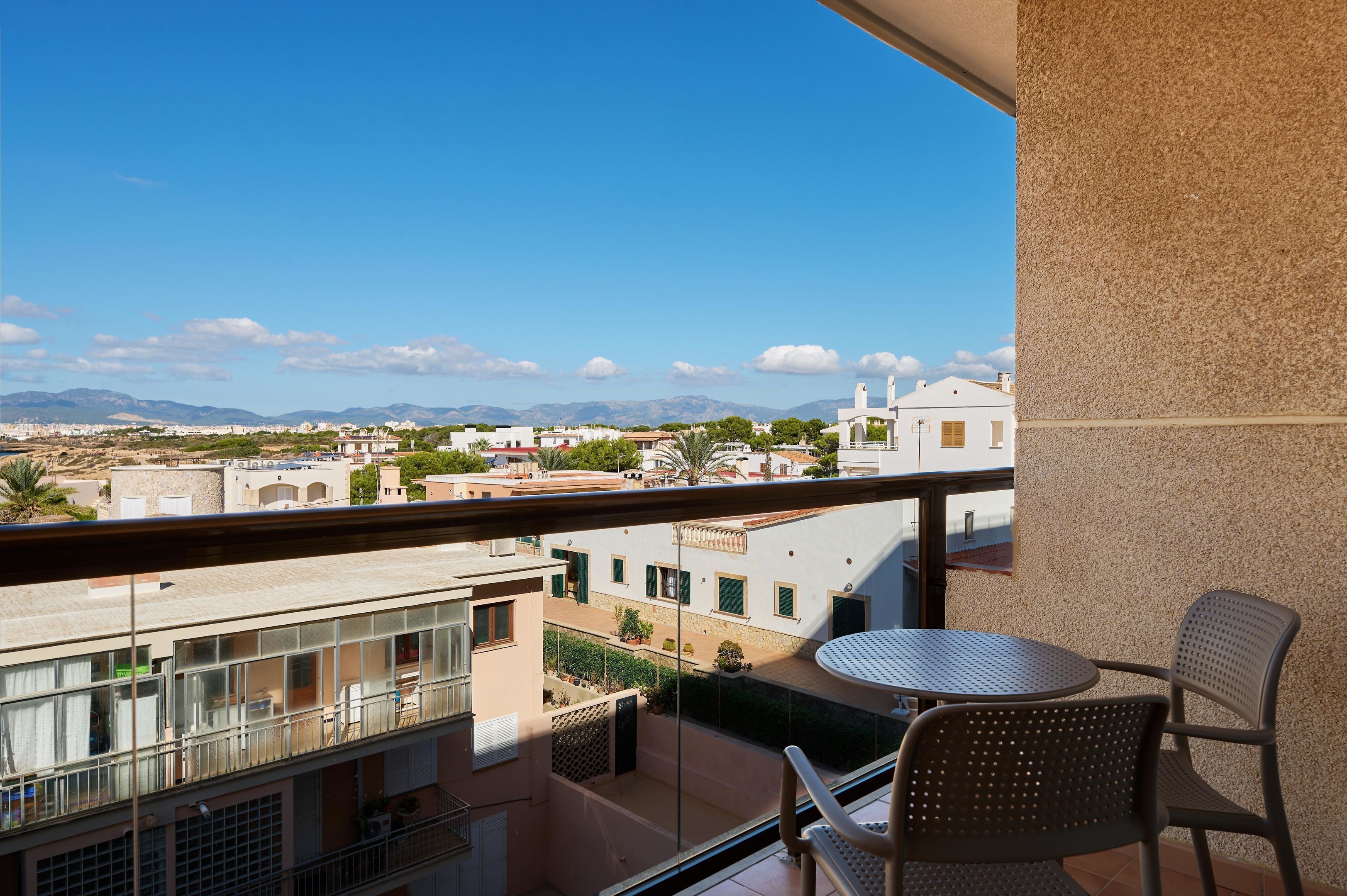 A balcony with a table and chairs, overlooking a cityscape with buildings and mountains.