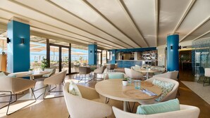 A spacious indoor area with round tables and chairs, a bar area, and large windows offering views. - AluaSoul Palma - Adults Only (Palma de Mallorca)