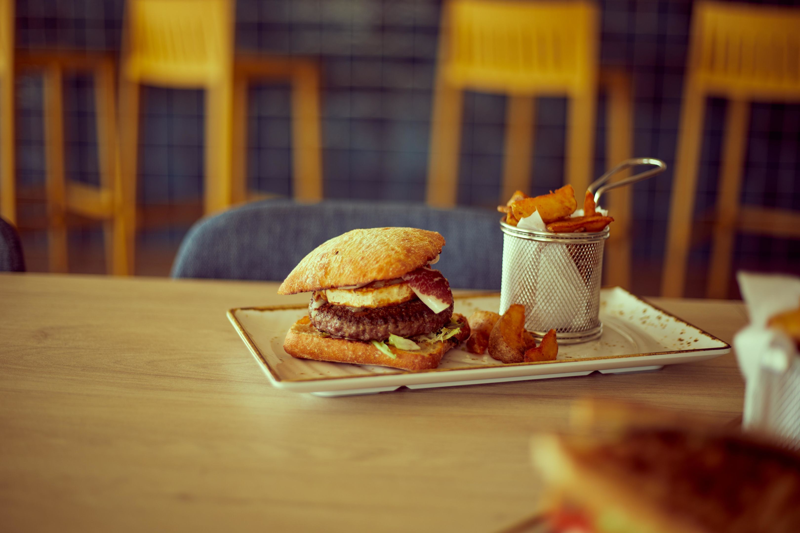 Ein Sandwich und Pommes auf einem Tisch, im Hintergrund Stühle.