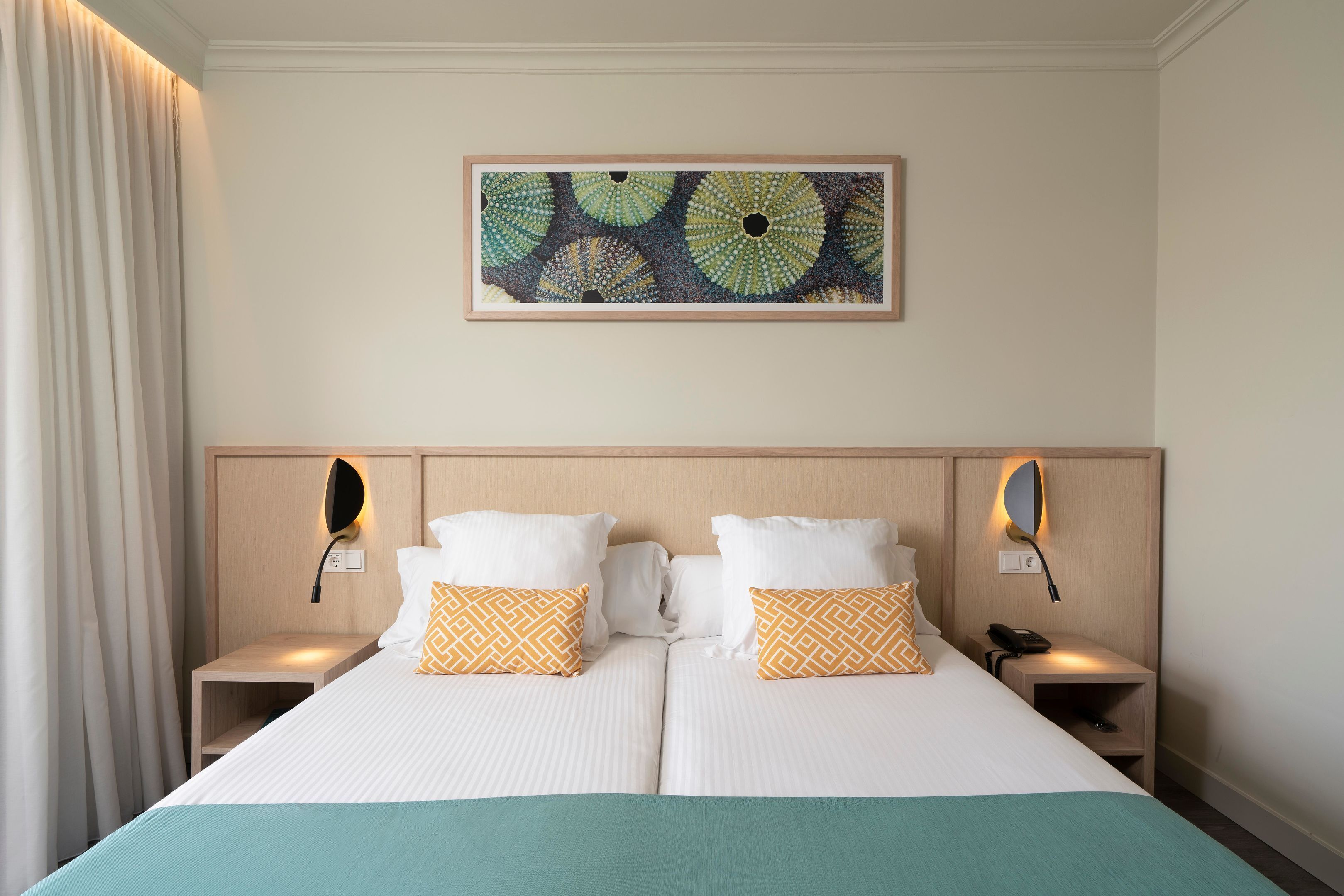 Una cama doble con dos almohadas, una mesita de noche con un teléfono y una obra de arte colgada en la pared.