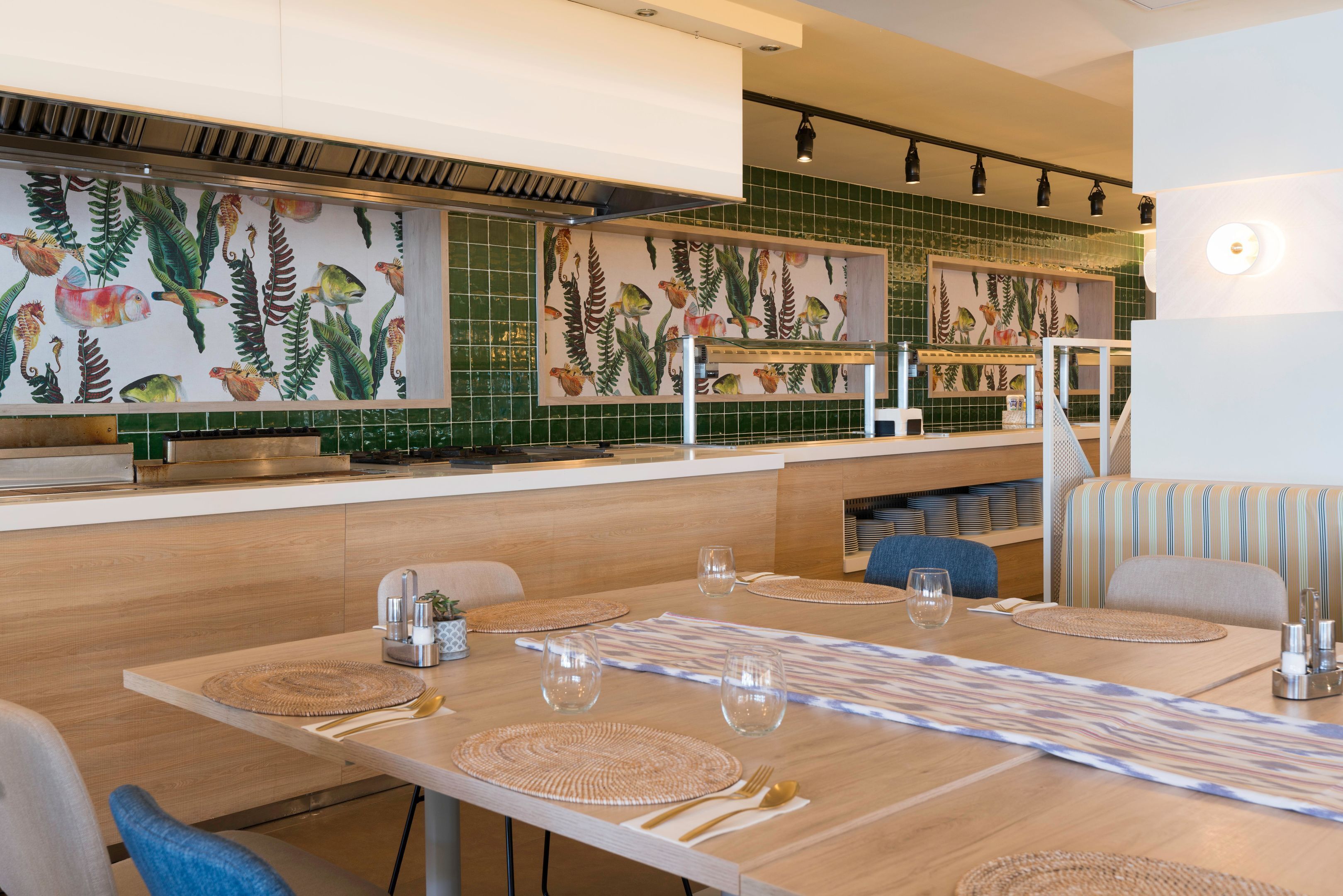 A restaurant with a long wooden table, chairs, and a counter with a green tiled backsplash.