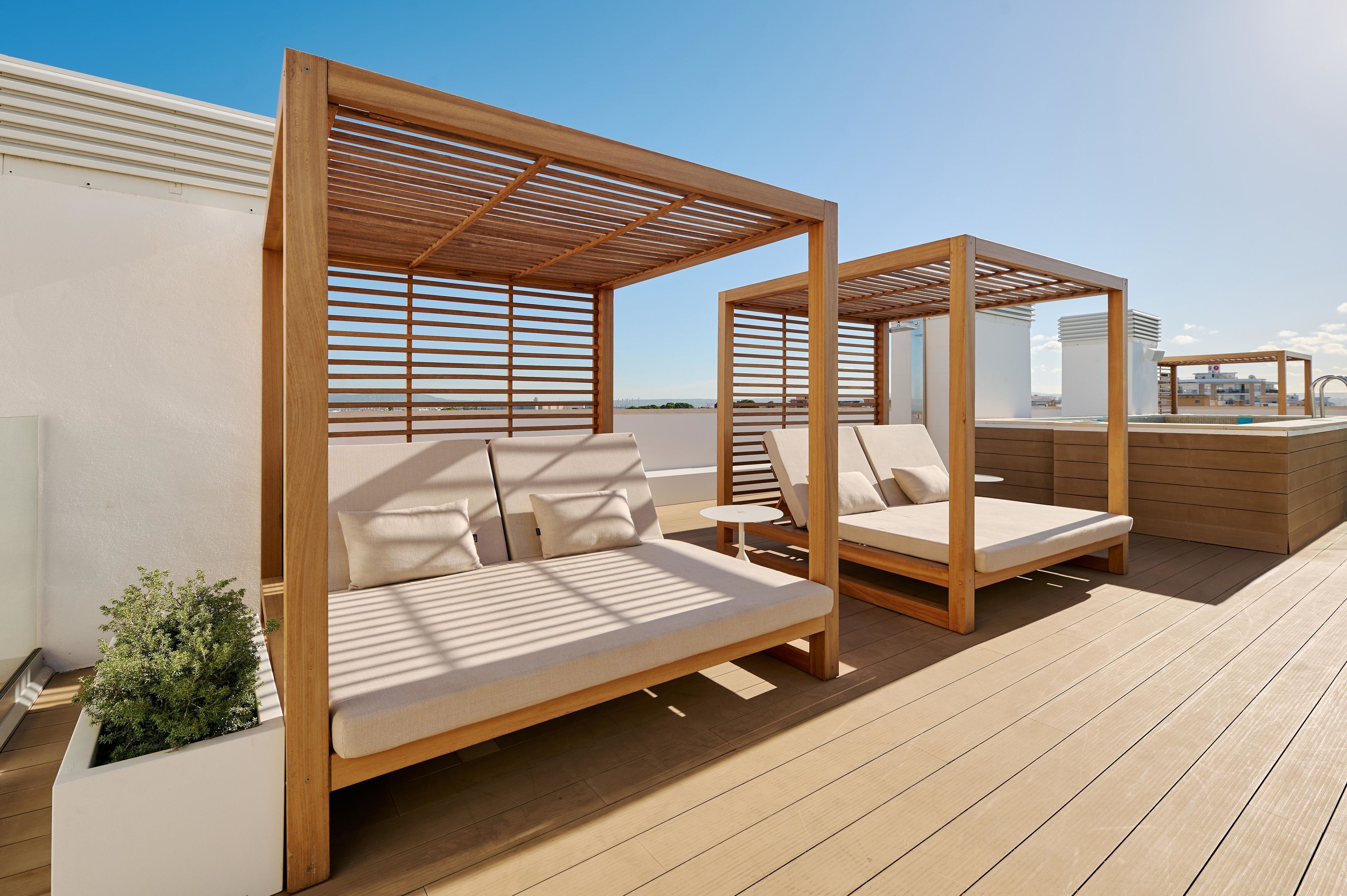 A rooftop deck with two wooden canopy beds, a small table, and a planter with greenery.