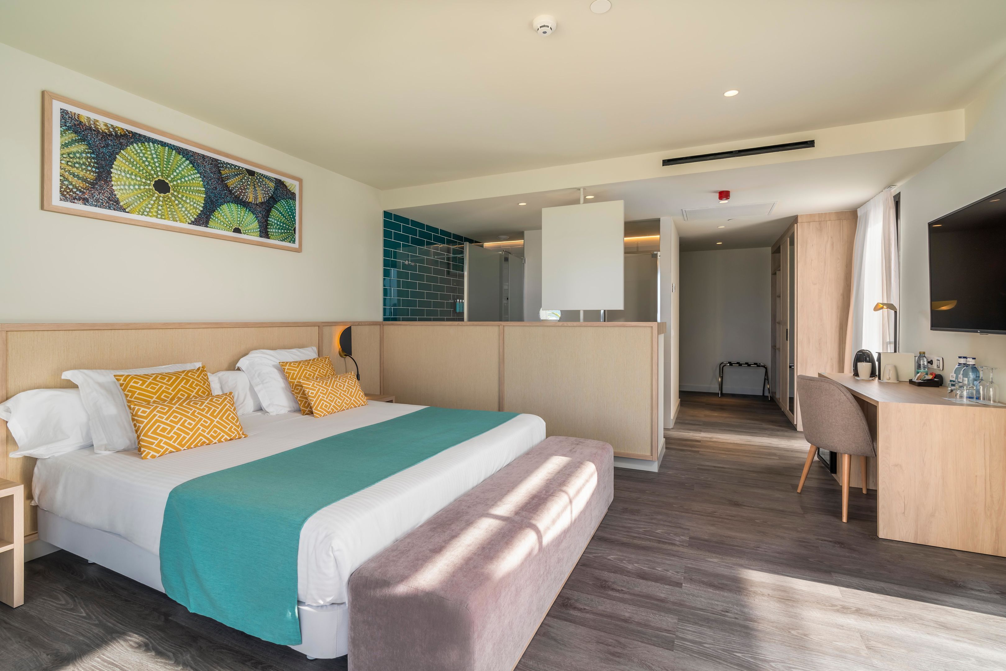 A modern hotel room with a large bed, a desk, a chair, a television, and a painting on the wall.