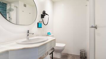 A modern bathroom with a round mirror, a sink, a toilet, and a hairdryer mounted on the wall.