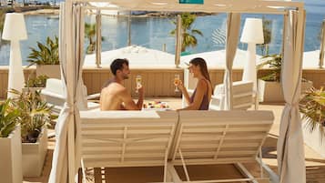 Un couple est assis à une table, face à la mer, entouré de fauteuils et de plantes en pot.
