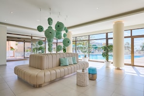 Eine moderne Lobby mit einem beigen Sofa, einem runden Couchtisch und einem großen Fenster mit Blick auf einen Pool.