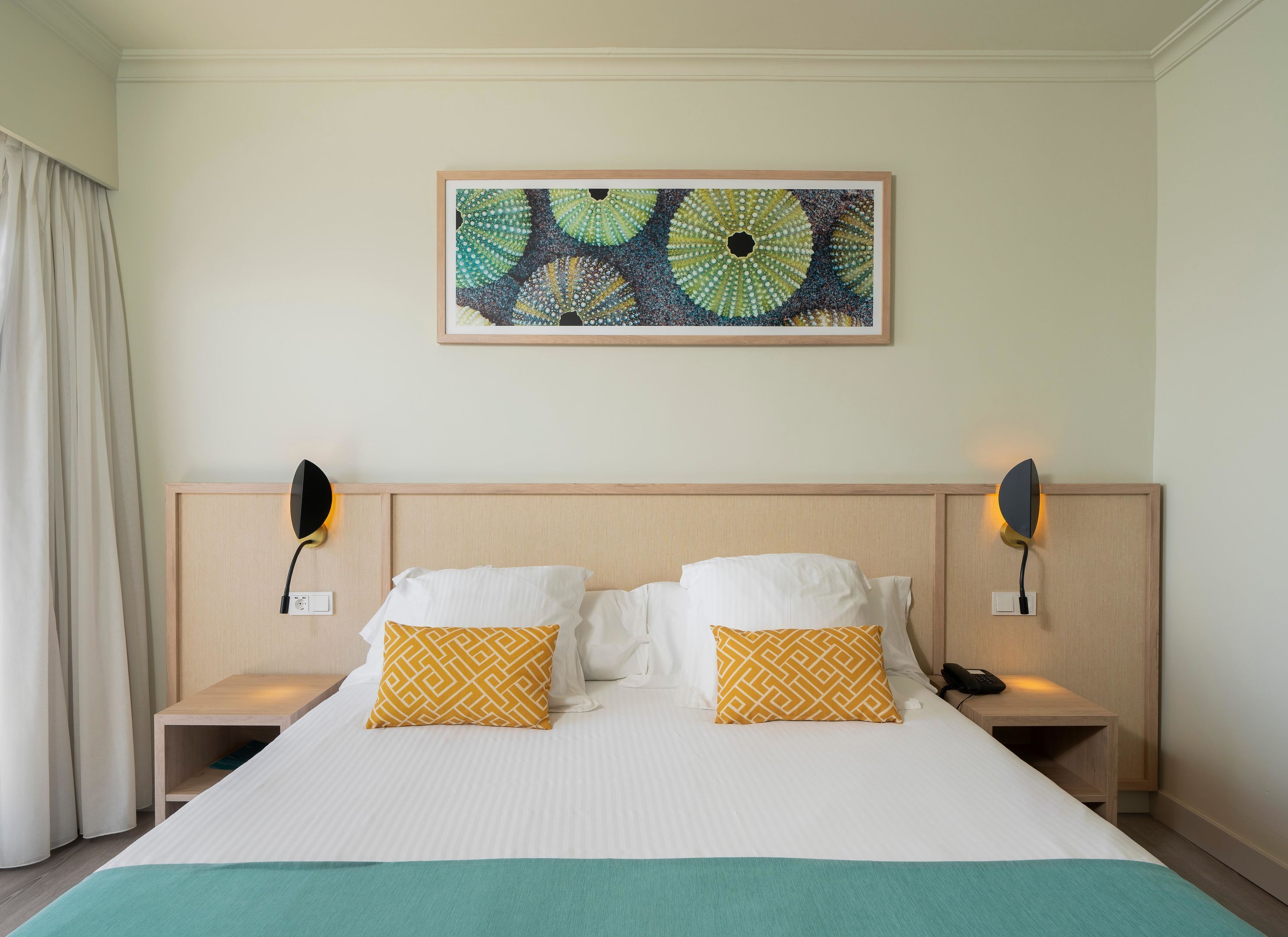 Une chambre d’hôtel avec un grand lit, deux tables de chevet, une œuvre d’art accrochée au mur et une fenêtre avec des rideaux.