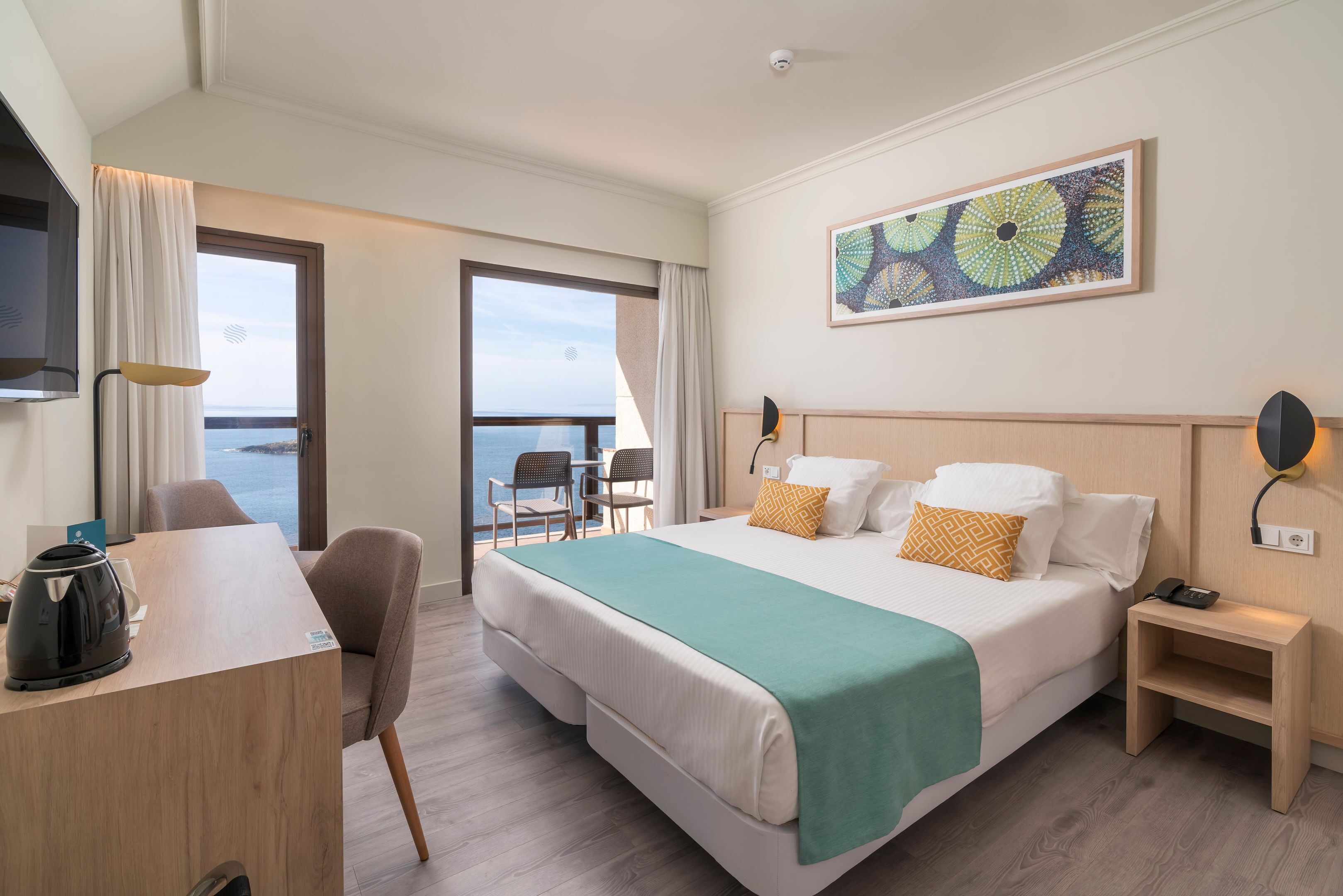 Hotelkamer met een bed, bureau, stoel, nachtkastje, lamp en groot raam met uitzicht.