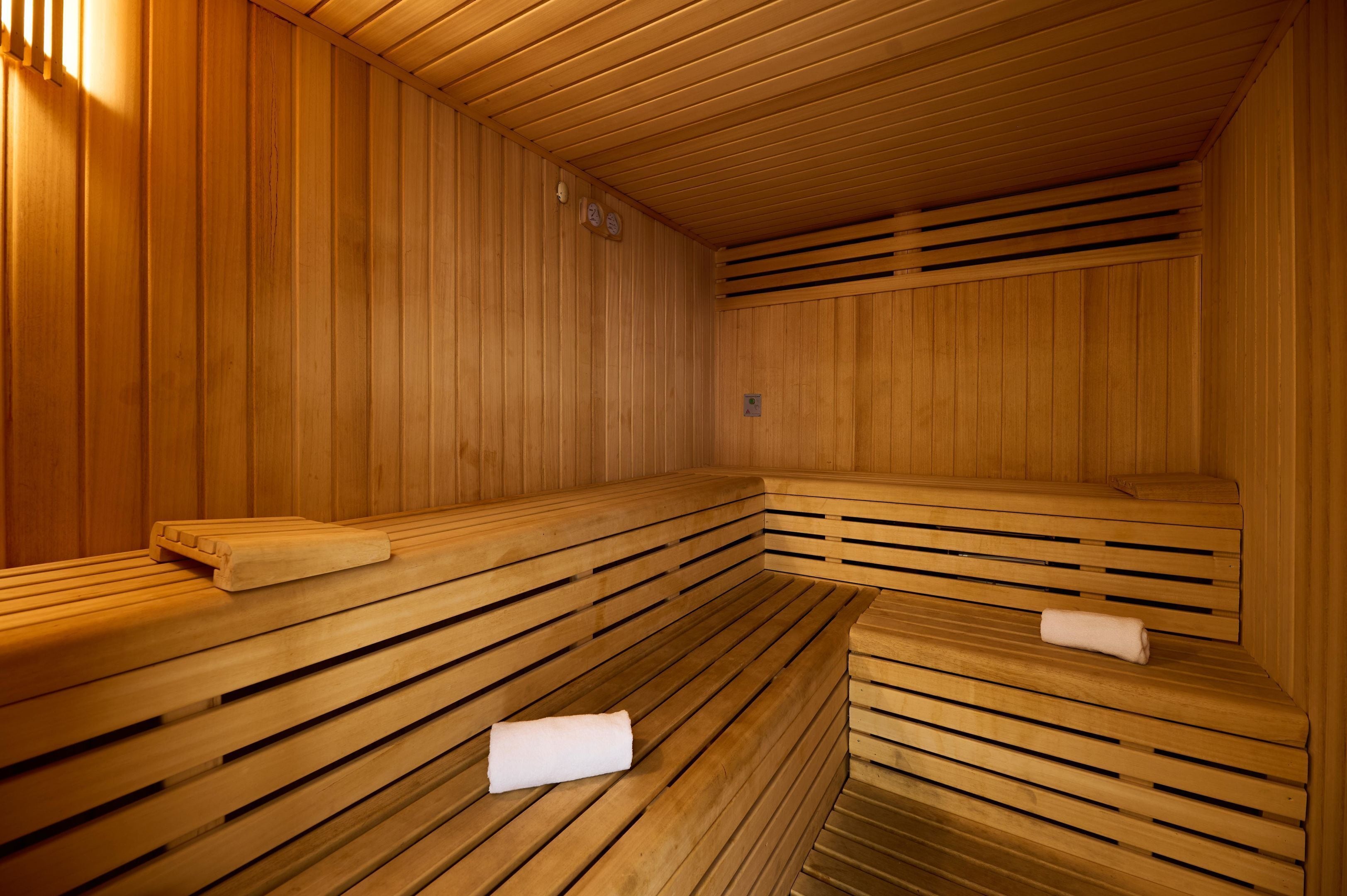 Un sauna avec des bancs en bois, une serviette sur le sol et une horloge au mur.