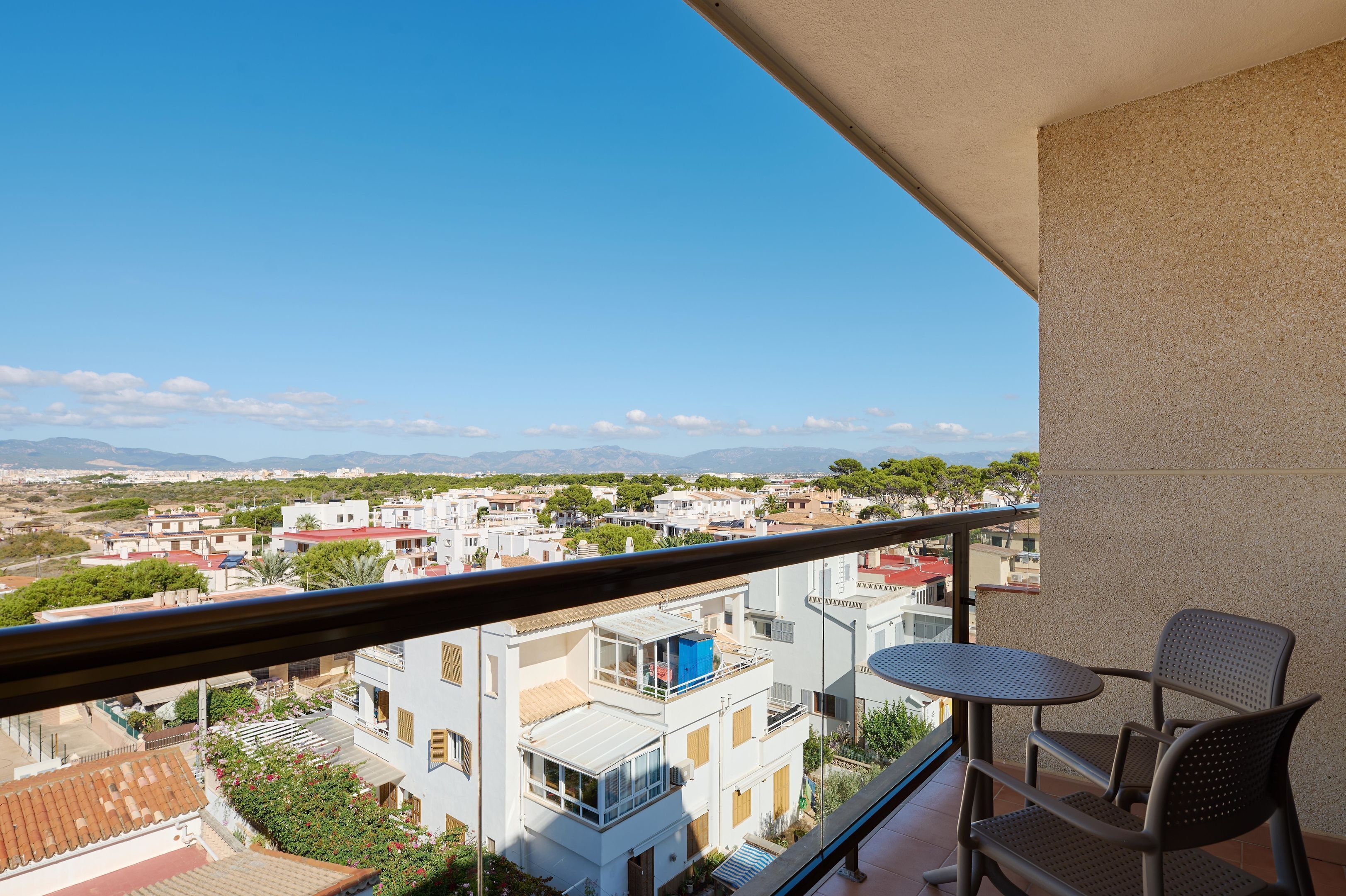 A balcony with a table and chairs, overlooking a residential area with buildings and greenery.