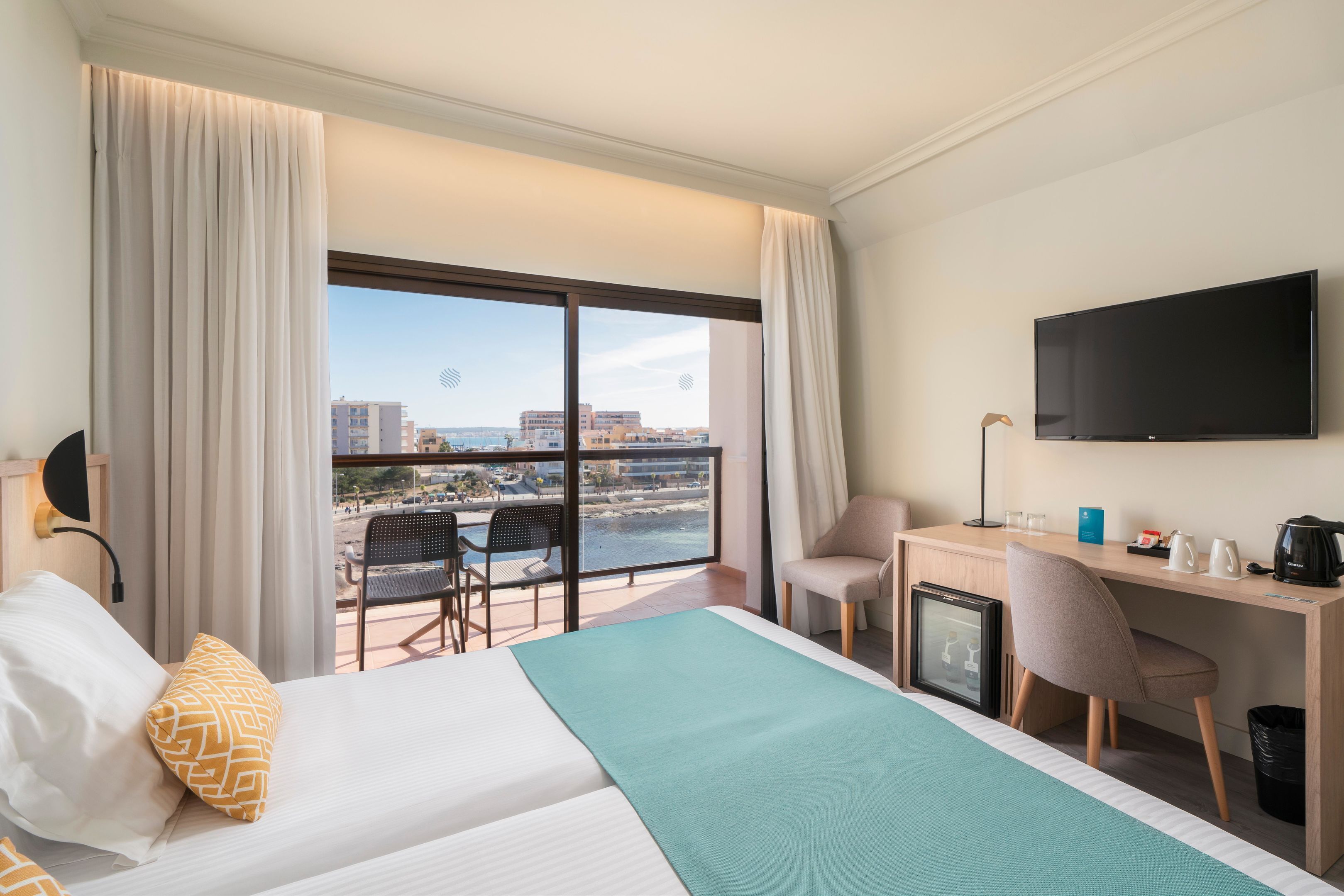 Habitación de hotel con cama, escritorio, silla, televisor y balcón con vista a la ciudad.